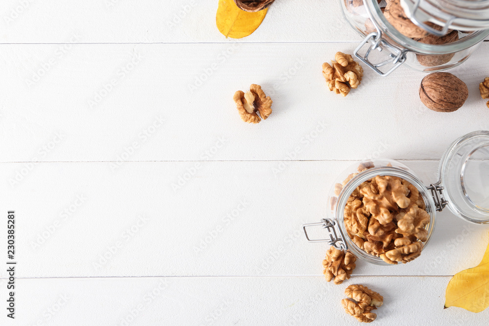 Glass jars with shelled walnuts on white table