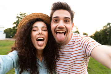 Poster - Image of beautiful couple man and woman 20s walking in green park, and taking selfie on cell phone