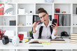 © Ivan Traimak - A young girl sits at a computer desk in the office and holds a bank card and phone.