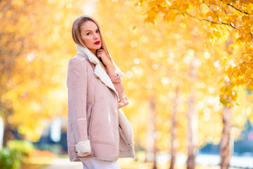 Fall concept - beautiful woman drinking coffee in autumn park under fall foliage