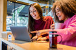 © Davide Angelini - Multiracial girls smiling using a laptop drinking coffee at the bar