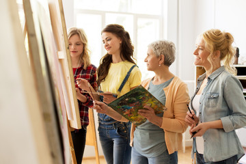 Sticker - creativity, education and people concept - group of female artists or students with brushes and palettes and teacher painting on easel at art school studio