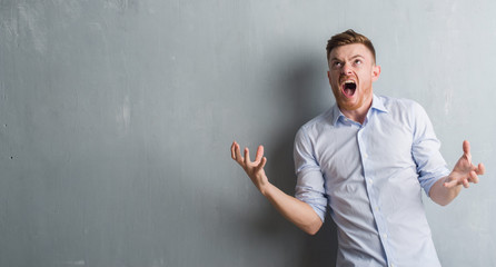 Wall Mural - Young redhead business man over grey grunge wall crazy and mad shouting and yelling with aggressive expression and arms raised. Frustration concept.