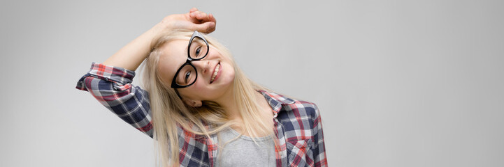 Beautiful teen girl with long hair and wearing glasses. A teenage girl in a plaid shirt and a gray T-shirt. A teenager girl put her hand behind her head.