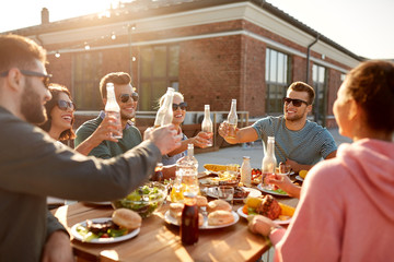 Poster - leisure and people concept - happy friends toasting drinks dinner or barbecue party on rooftop in summer