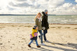 family, leisure and people concept - happy mother, father and little son walking along autumn beach with picnic basket and blanket