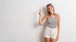 © Krakenimages.com - Young beautiful blonde woman over white brick wall showing and pointing up with fingers number three while smiling confident and happy.