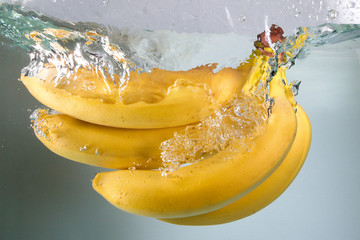 Bunch of bananas splashing in water on white