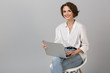 © Drobot Dean - Young business woman posing isolated over grey wall background sitting on stool using laptop computer.