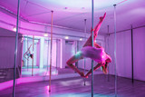 Fototapeta  - Strong but graceful. Strong but graceful pole dancer training hard in big and light studio with mirror