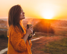 Young Woman  In A Orange Sweater With Thermos Thermo Cup Outdoor Portrait In Soft Sunny Daylight. Autumn. Sunset. Cozy