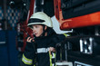 portrait of female firefighter in protective uniform talking into  portable radio set at fire station