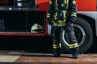 partial view of female firefighter in protective uniform standing near truck with helmet at fire station