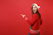 Back Rear View Of Shocked Santa Girl Looking Back, Keeping Mouth Wide Open, Looking Surprised, Pointing Index Finger Isolated On Red Background. Happy New Year 2019 Celebration Holiday Party Concept.