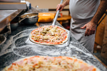 Chef taking raw pizza on metal shovel for baking in the oven.