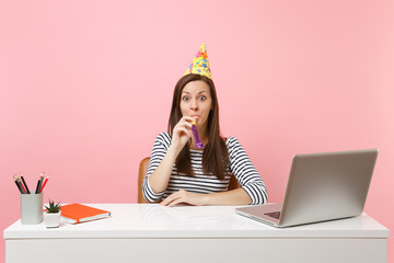 Wall Mural - Young shocked woman in birthday party hat with playing pipe celebrating while sit work at white desk with pc laptop isolated on pastel pink background. Achievement business career concept. Copy space.