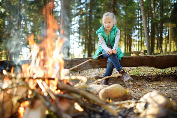 Wall Mural - cute little girl roasting hotdog on a stick at bonfire. child having fun at camp fire. camping with 