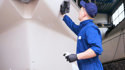 Young handsome professional guy (male) cleaner, washes the yacht after polishing and lining ceramics on the yacht. Concept of: Ceramics, Cleaning, New Ship, Polishing, Cleaner, In Robe, Cap, Hard Work