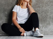 cropped shot of girl in jeans sitting on floor near grey wall