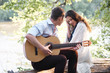© soleg - young couple sitting on a log by the river and playing guitar, summer nature, bright sunlight, shadows and green leaves, romantic feelings