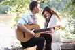 © soleg - young couple sitting on a log by the river and playing guitar, summer nature, bright sunlight, shadows and green leaves, romantic feelings