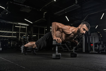 Young handsome male athlete bodybuilder weightlifter with idial abdominals, doing exercises in modern gym on a dark background. Exercises for biceps. 