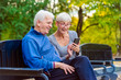 © lordn - Smiling senior active couple sitting on the bench looking at smartphone
