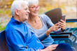 © lordn - Smiling senior active couple sitting on the bench looking at smartphone