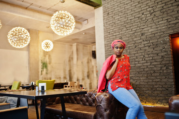 Wall Mural - Stylish african woman in red shirt, jacket and hat posed indoor cafe.