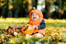 Child In Pumpkin Suit On Background Of Autumn Leaves