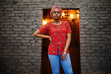 Wall Mural - Stylish african woman in red shirt and hat posed against brick wall.