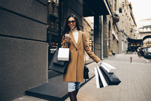 Shopping. Black Friday. Technology. Woman With Shopping Bags Is Using A Smartphone And Smiling While Walking Down The Street
