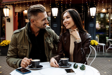 Wall Mural - Autumn walk. Cafe. Couple. Love. Man and woman in warm casual clothes are drinking coffee, talking and smiling while sitting in the cafe outdoors