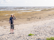 Senior Man With Binoculars Looking At Tidal Flats At Low Tide Of Waddensea From Beach Of Boschplaat On Terschelling, Netherlands