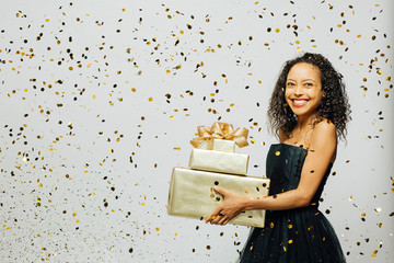 Very happy with the gifts, portrait of a woman in a black dress with a big smile holding gifts as gold confetti are falling