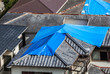High angle view of houses hit by natural disaster, with damaged tiled roof covered with blue tarp