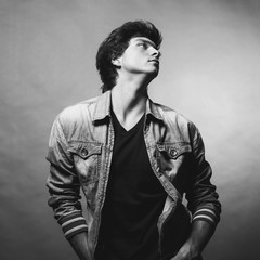 Wall Mural - Portrait of Handsome Young Man. A Men in a Denim Jacket Posing on a Gray Background. Black and White Photo