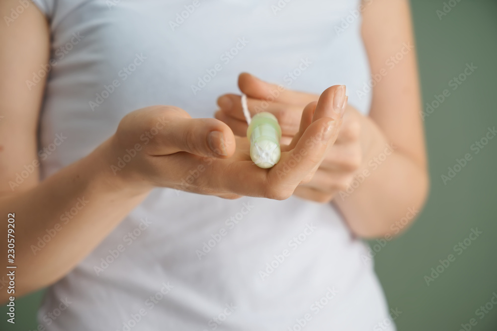Woman holding tampon on color background, closeup