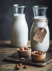 Two bottles of almond, gluten fre milk and wooden bowls with almonds on rustic wooden table. Paper label with words: almond milk on the bottle.