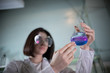 © KONSTANTIN SHISHKIN - Chemical laboratory. Young woman holding a flask with blue and purple exfoliating liquid in it