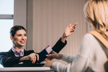 Wall Mural - smiling airport worker showing route to young traveler at check-in desk