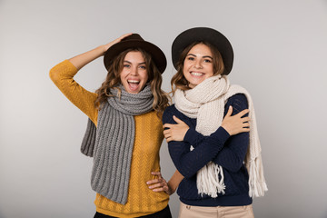 Sticker - Image of two adorable women wearing hats and scarfs smiling at camera, isolated over gray background