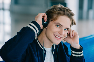 Wall Mural - happy young man in headphones smiling at camera in airport