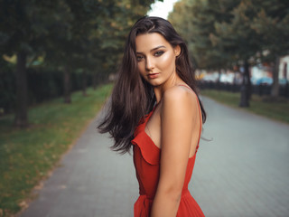 Fashion sensual woman portrait. Outdoor photo of attractive brunette model in red dress. Gorgeous brunette girl portrait in summer sexy red dress against evening city street. Shallow DOF