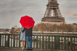 © Song_about_summer - autumn in Paris, couple under red umbrella near Eiffel tower, fall season, love in rainy day, romantic moment on the bridge