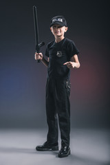 preteen boy in policeman uniform with truncheon on dark backdrop