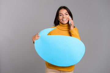 Sticker - Happy woman posing isolated over grey wall background holding speech bubble talking by phone.