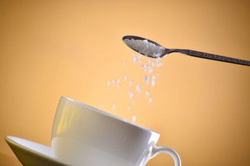 Wall Mural - sugar pouring in cup against brown background