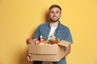 © New Africa - Young man holding box with donations on color background