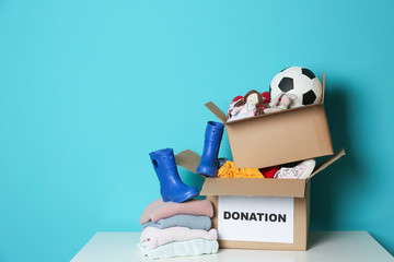 Wall Mural - Donation boxes with toys, knitted clothes and shoes on table against color background. Space for text